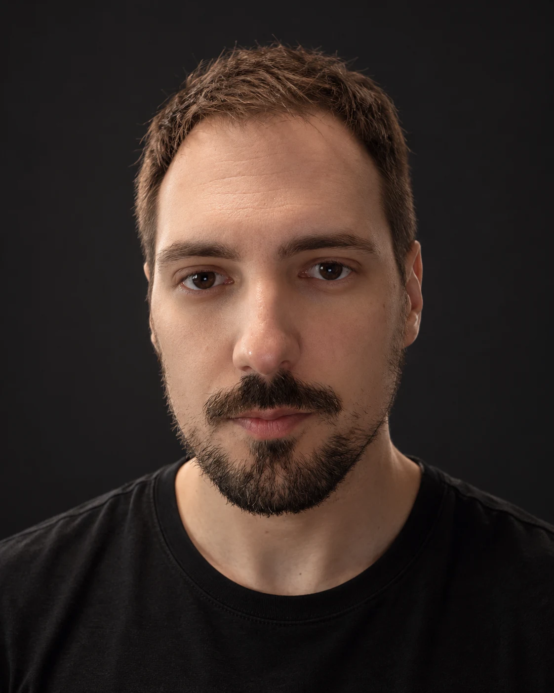 Portrait of George Theodorou in a black shirt against a dark background.